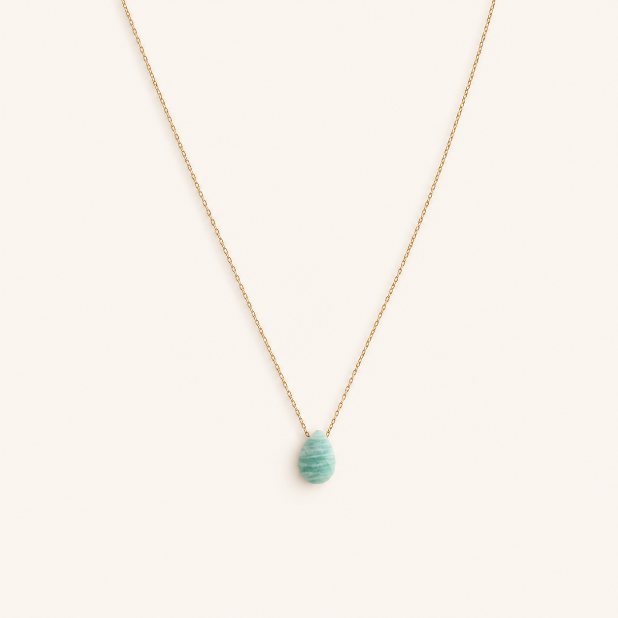 Naïa, collier doré à pendentif goutte turquoise sur fond beige ivoire